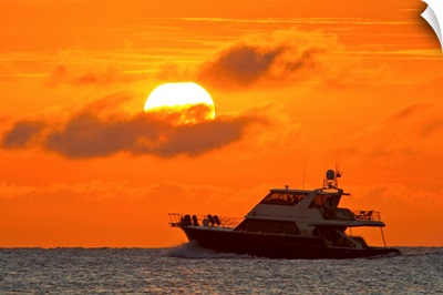 Boat passing in front of a big glowing sun during a spectacular sunset