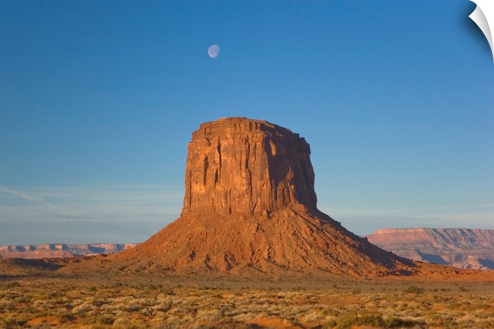 Moon visible over rock formation in Monument Valley in early morning.