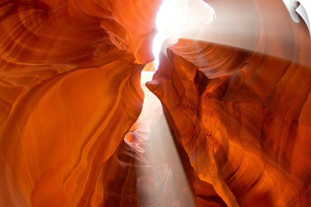 Rays of sunshine come through the cracks of a canyon as the photograph is taken looking up at them.