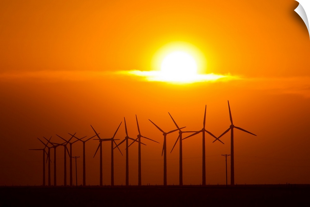 The sun sets behind a row of spinning windmills or wind turbines.