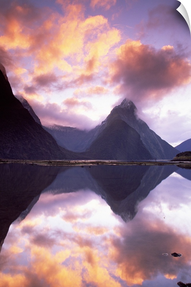 Big, vertical photograph of Mitre Peak, reflecting in the still water of Milford Sound, as the sun sets in a vibrant, colo...