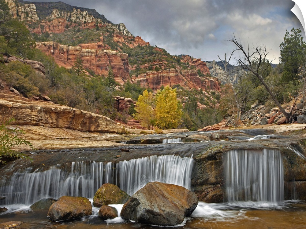 Wall art of a small waterfall in a river with red rock formations in the background.