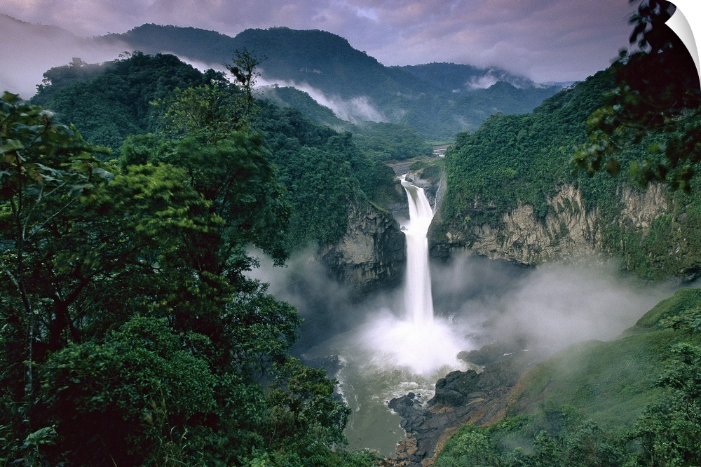 Photograph of waterfall surrounded by rainforest with mountain silhouette in the distance.