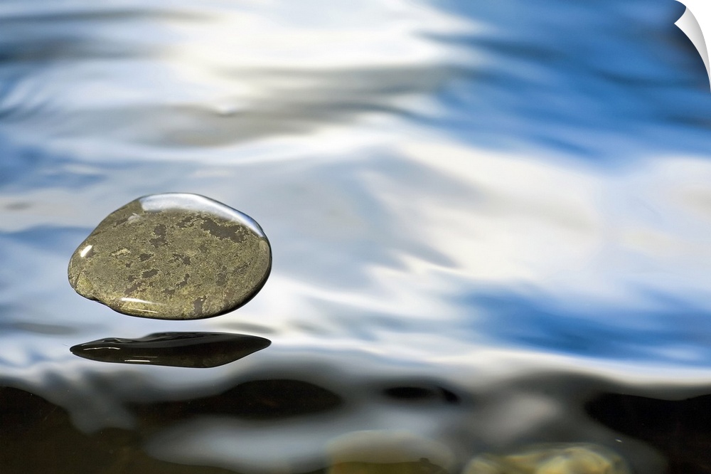 A rock just about to hit the water's surface. The surface tension of the liquid keeps the pebble encased as it hovers over...