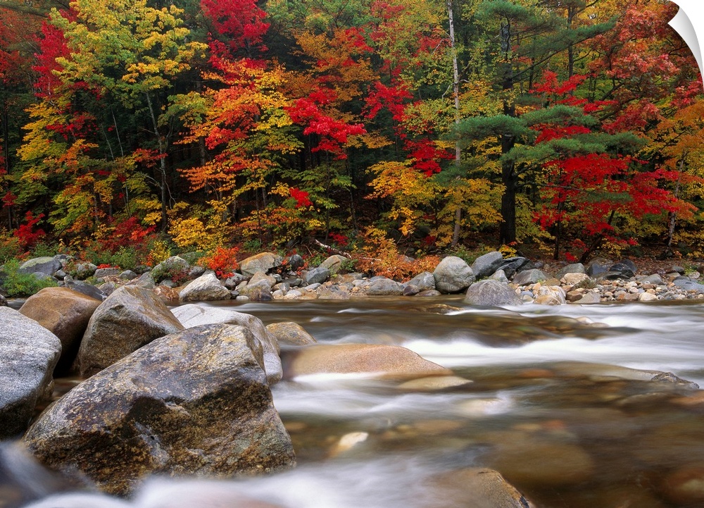 A time lapsed photograph of a boulder filed river with New England autumn trees growing on the shore.