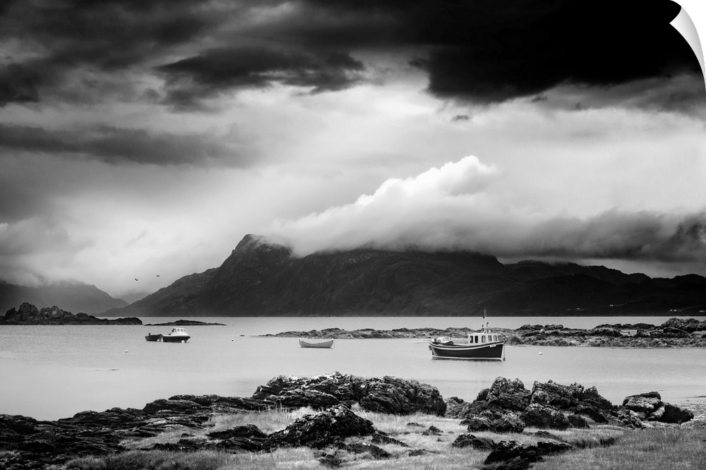 Black and white landscape photograph of a cloudy sky over a mountainous lake with boats.
