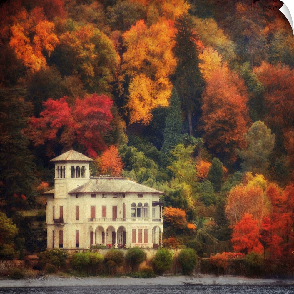 This is a landscape photograph on square shaped wall docor that shows a lake side villa surrounded by a forest of fall fol...