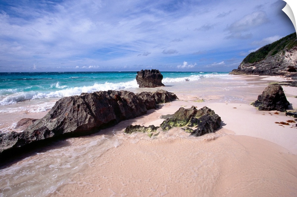 View of a Pink Sand Shore, Elbow Beach, Bermuda, large rocks half-buried in the sand and foamy waves coming in from the oc...