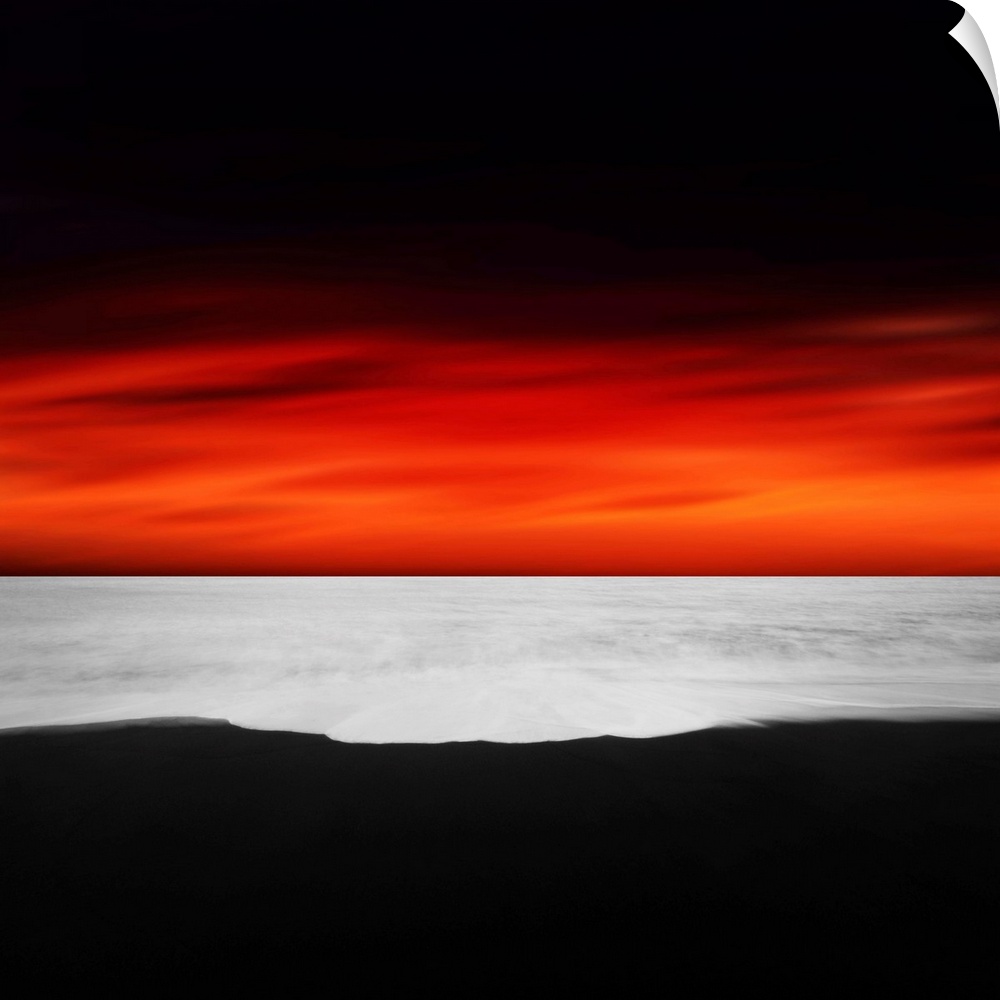 A dramatic photograph of a blazing sky hanging over a white seascape seen from a black sand beach.