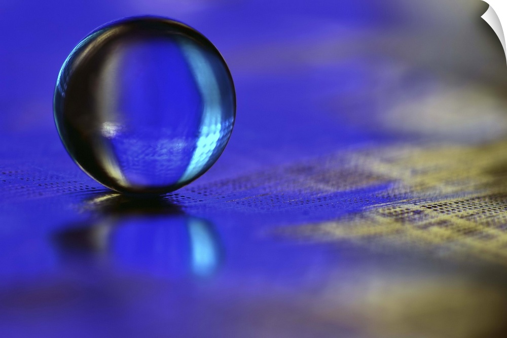 A macro photograph of a water droplet sitting o a blue surface.
