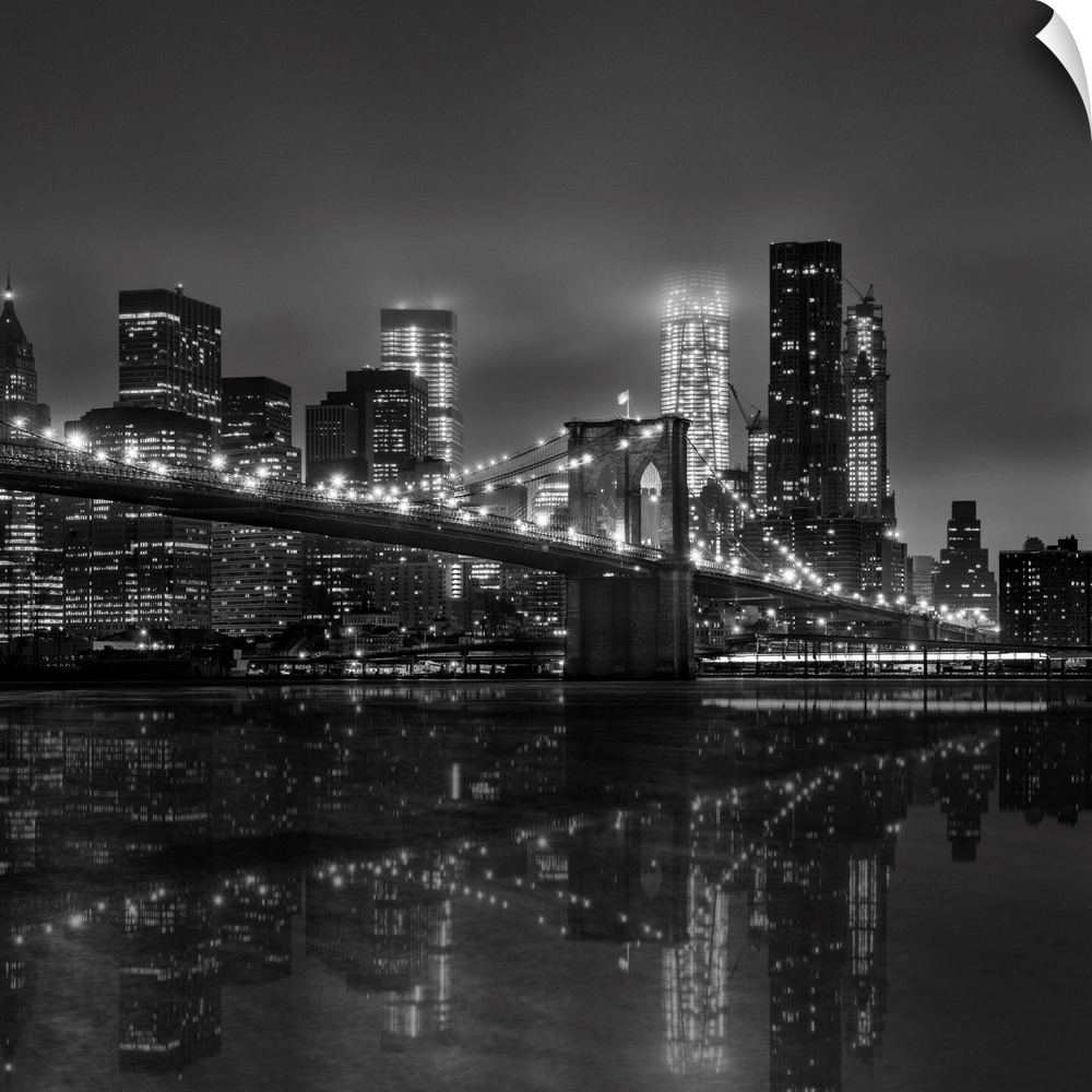 Black and white photograph of New York city's skyline at night with the Brooklyn bridge in the foreground.