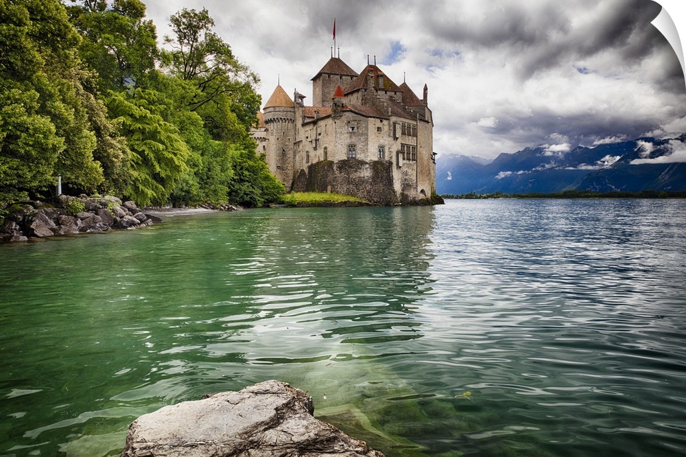 The Chateau de Chillon on the edge of Lake Geneva, with the Alps in the distance on a cloudy day, Switzerland.