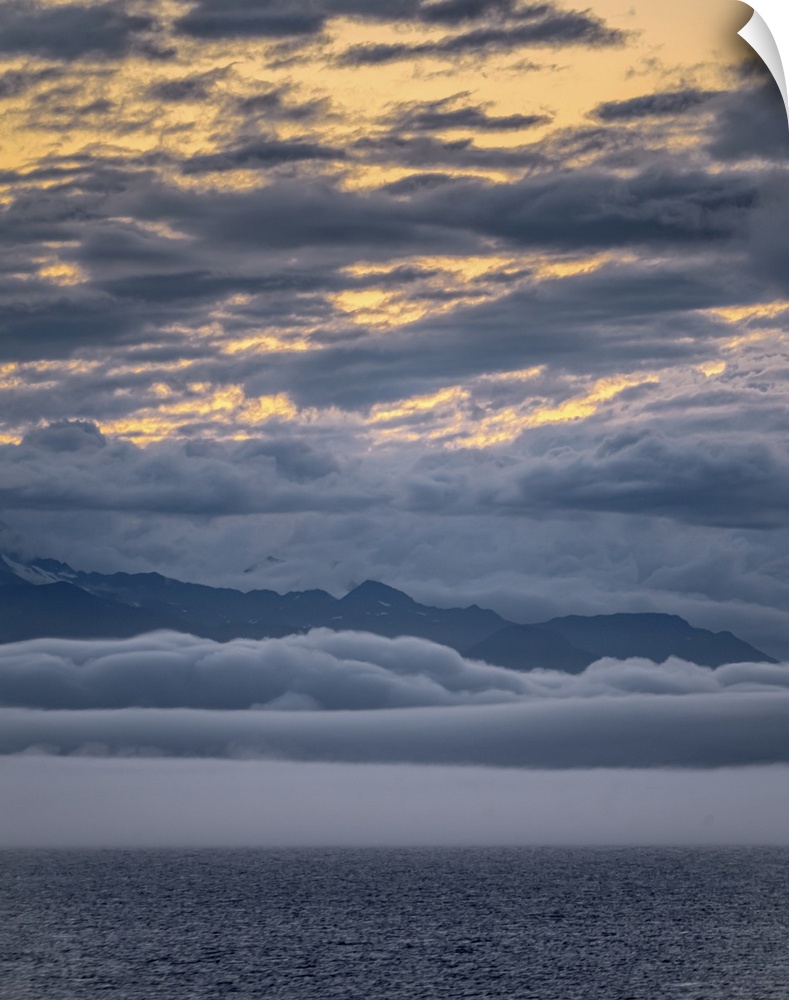 Peaceful snow-capped Alaskan mountain range at ocean's edge with clouds above and clouds below (cloud inversion) make for ...
