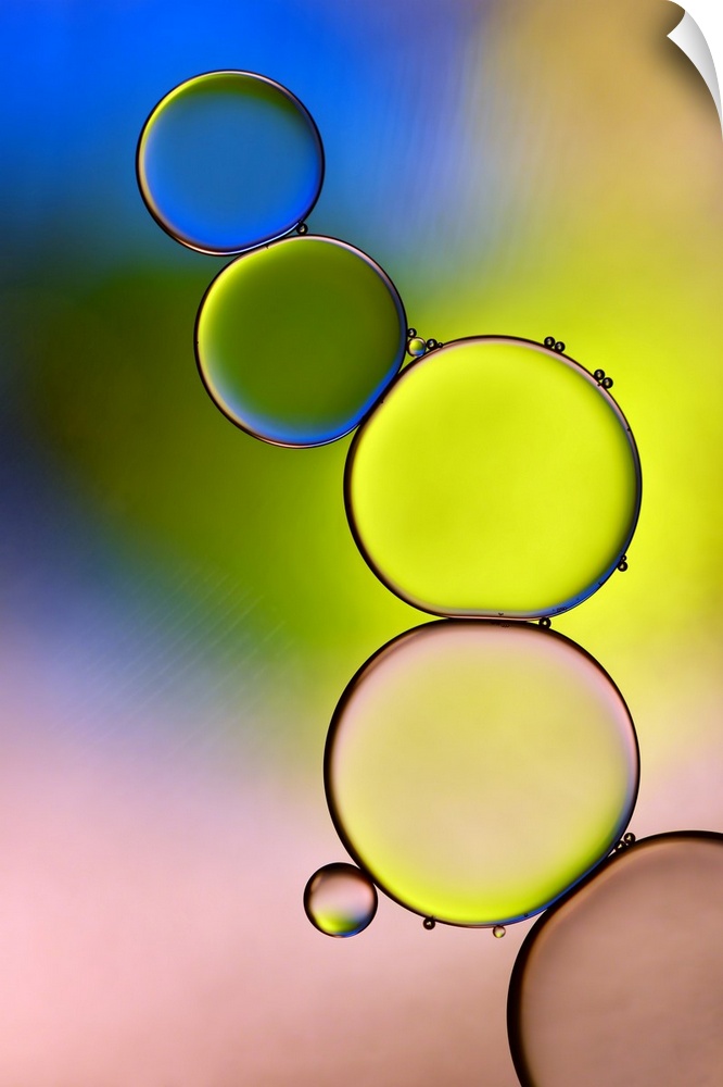 A stack of large water droplets with tiny droplets on top of them with green, yellow, blue, and pale pink hues.