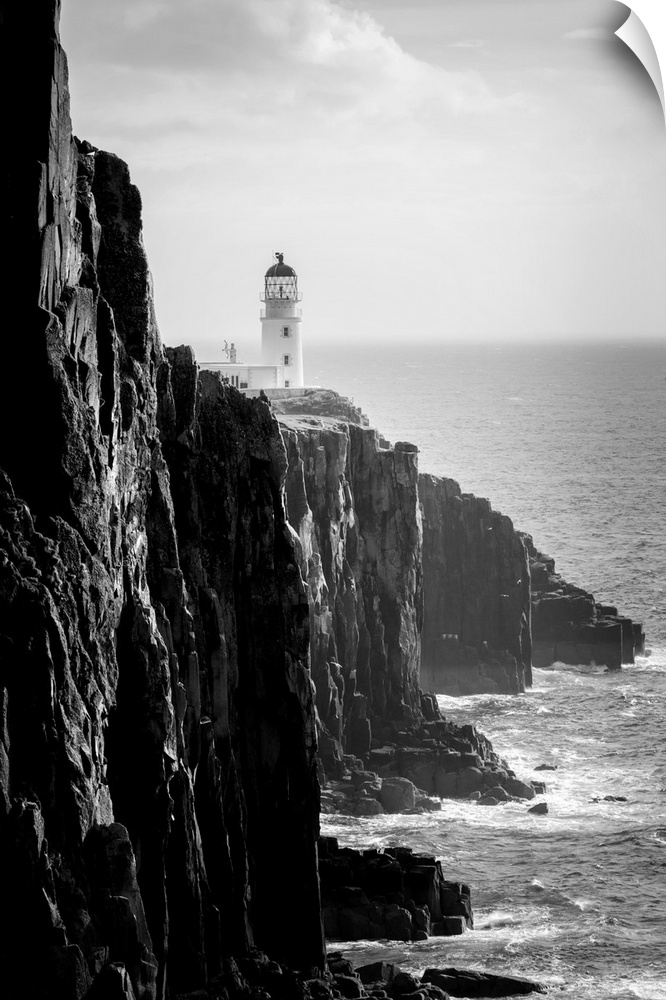 Fine art photo of a lighthouse at the edge of a cliff by the ocean in black and white.