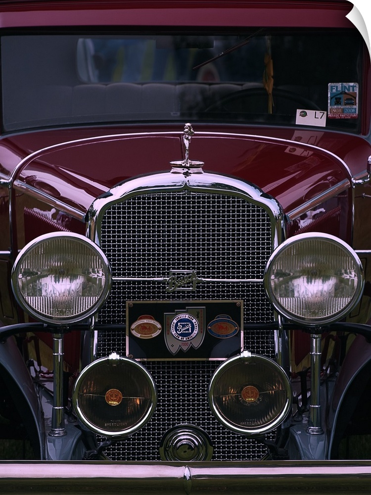The front grille and round headlights of a maroon colored vintage car.