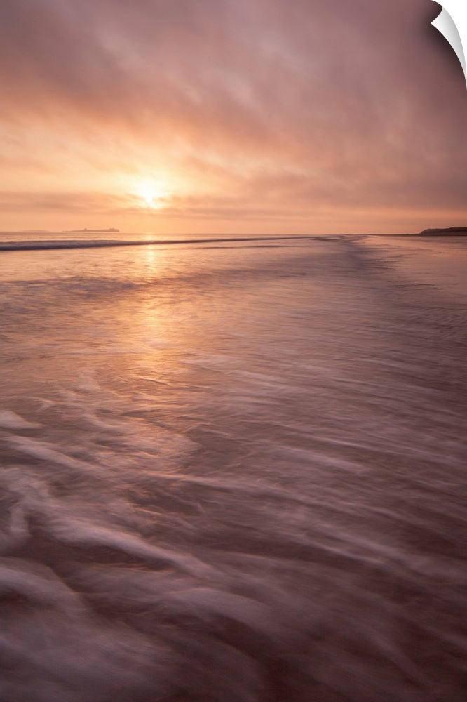 A calm saescape at dawn with a glowing peach sky reflecting in the sea with swooshing waves.