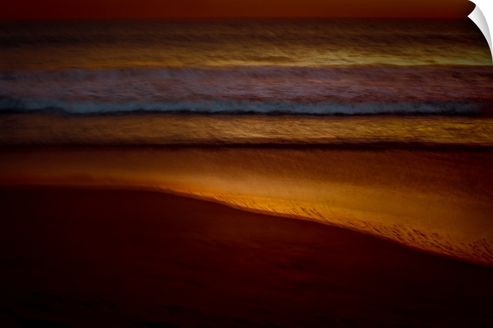 Golden lit photograph of ocean waves rolling on to the beach shore with a blurred look, created with a long exposure.