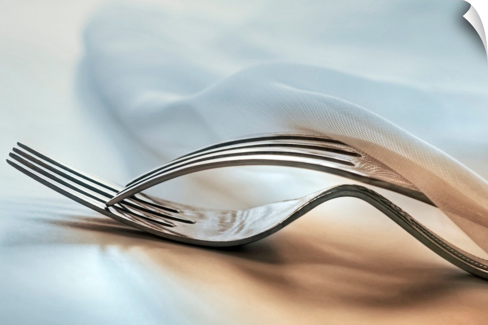 In this close up photograph two forks lie on top of each other under a napkin on a table.