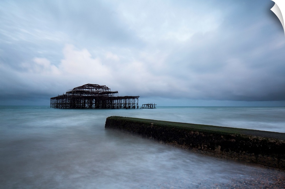 A cool blue dramatic storm image of Brighton Pier, Sussex, UK with the Old Pier in stormy seas and a concrete jetty in the...