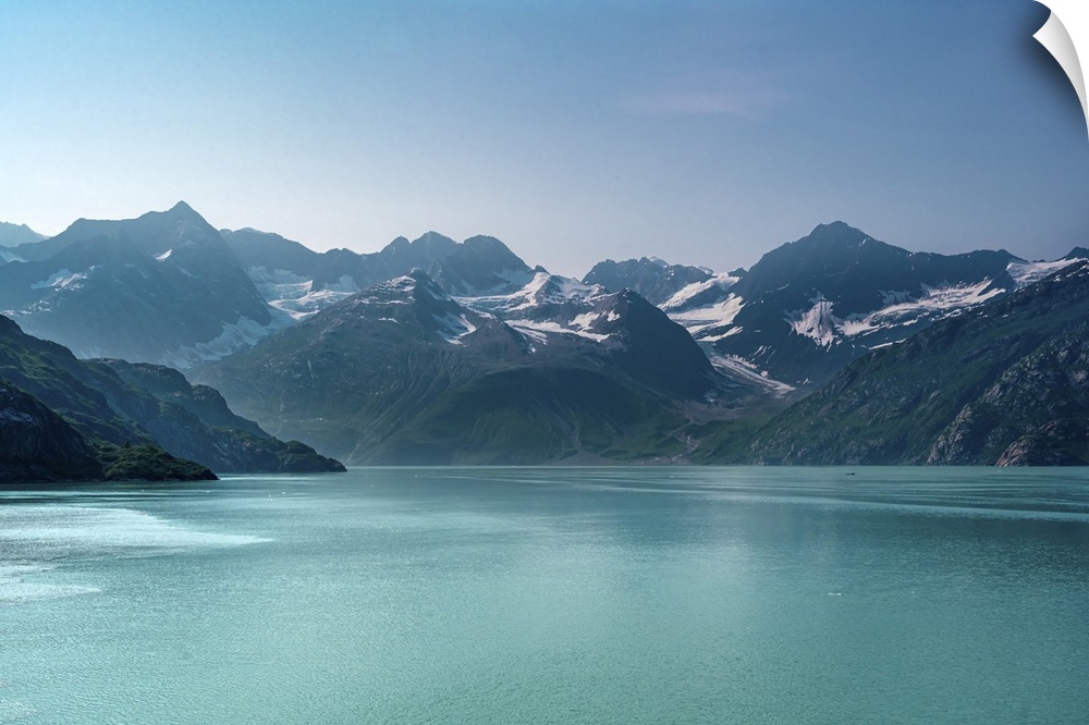 Beautiful Alaskan mid-morning scene of snow capped mountains rising out of luminous aquamarine blue glacier waters.
