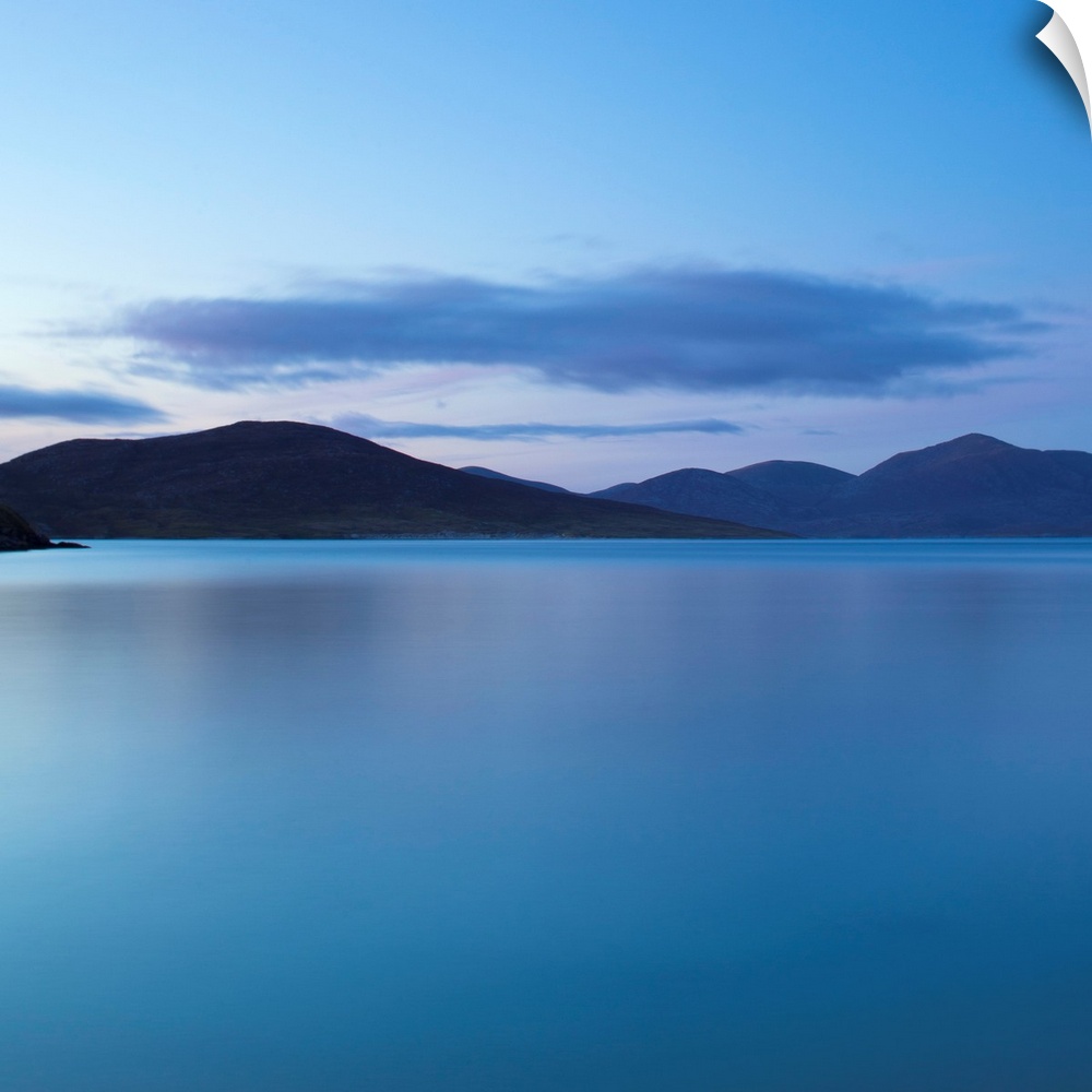 A cool blue minimal zen-like seascape of flat calm water with silhouetted mountains.