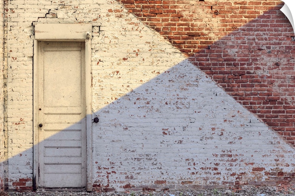 Photograph of an aged brick wall with a white door, angled paint lines, and an angled shadow on half of the image.