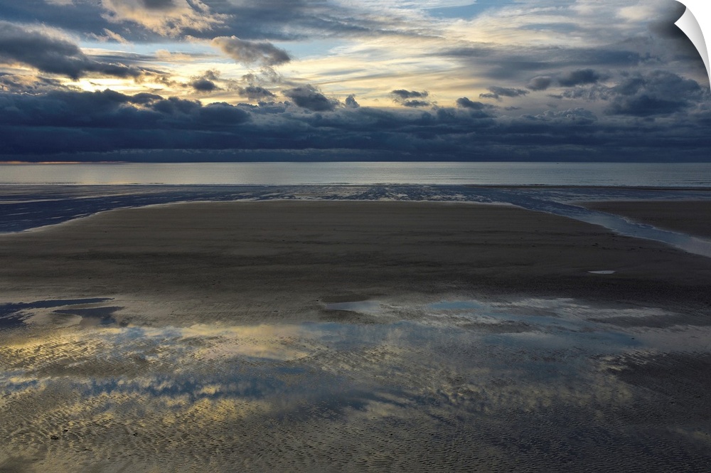 Landscape photograph of an empty beach on a cloudy day with the sky reflecting onto the puddles in the sand.