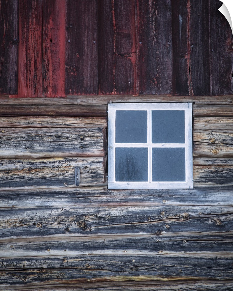 A close-up of an old white window ina weather Norweigian wooden building in the snow with grey and deep red timbers.