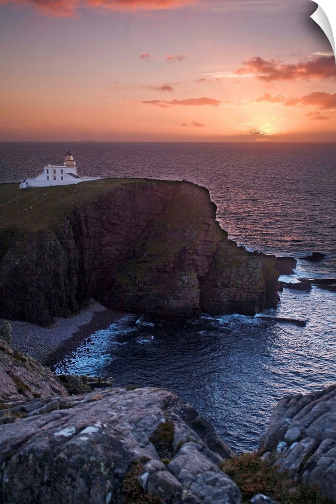 A sunset seascape over Neist Point Lighthouse, Isle of Skye, Scotland with a peach and gold sky.