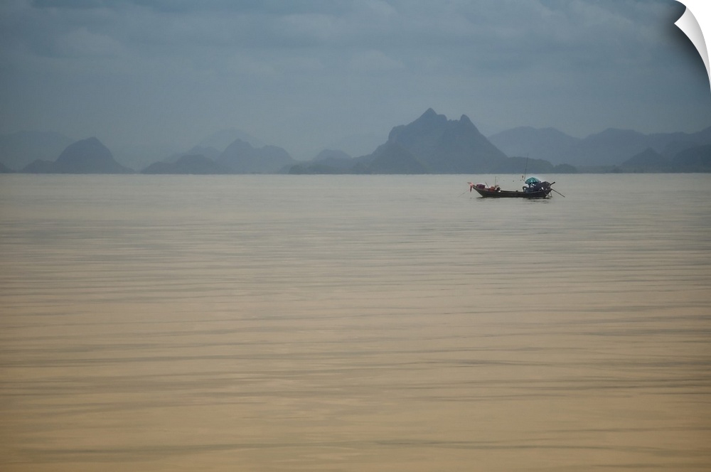 Single fishing boat in Thailand sea in the area of the Kho Phi Phi islands with mountains away, a blue and grey mood.
