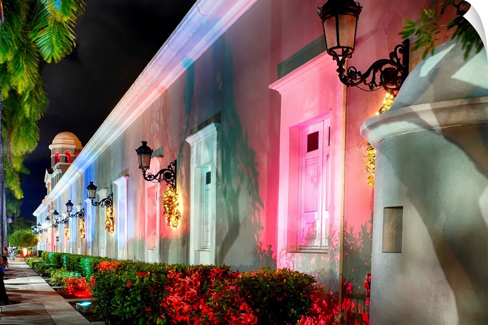 The side of a Spanish style building illuminated in varying colors for Christmastime.