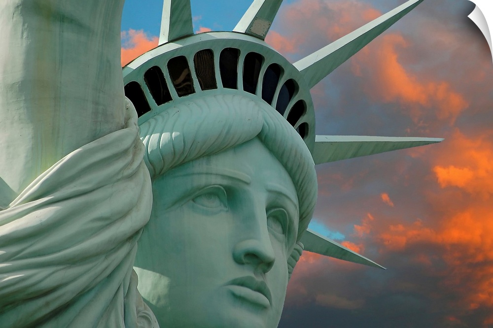 Artistic photograph of the face and crown of the Statue of Liberty in New York with a stunning sunset glow behind her.