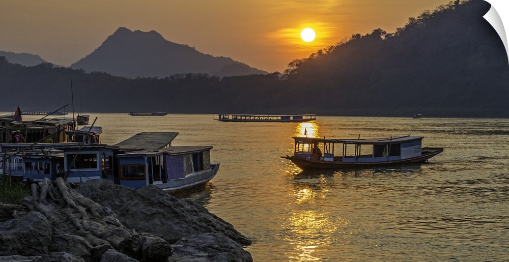 The sun low in the sky over fishing boats on the river in a valley in Laos.