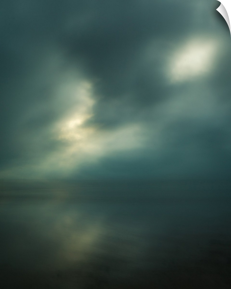 Dream-like photograph of a calm ocean with the sun starting to peak through a cloudy sky.