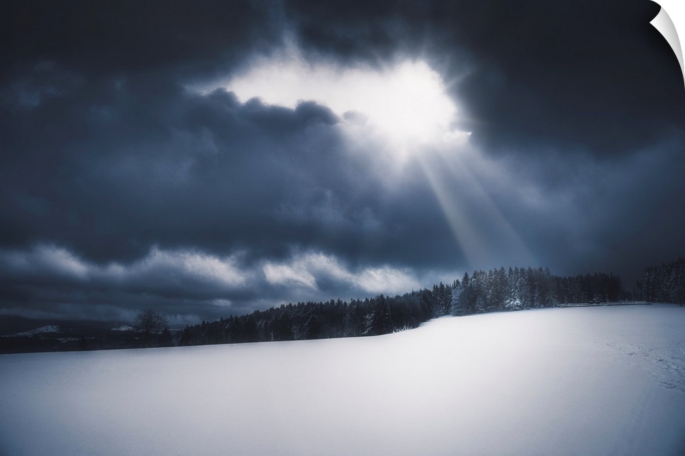 Snowy landscape lit by the sun piercing a stormy sky