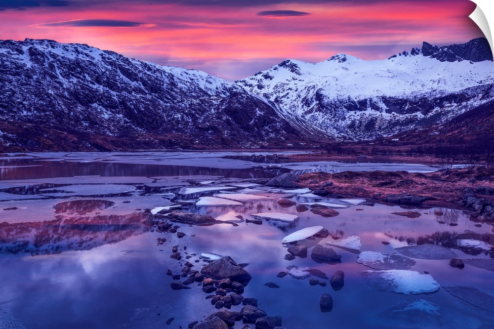 Snowy mountains in Lofoten, Norway, by a glacial lake at sunset.