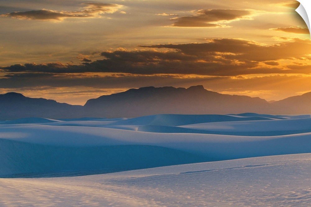 Large landscape photograph of the sun setting in a cloudy sky, over the Gypsum dunes, White Sands National Monument, in Ne...