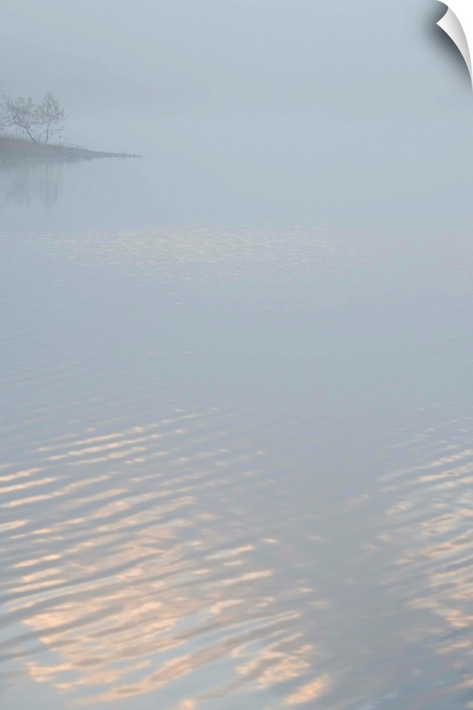Fine art photo of a lake covered in fog in the morning, with a little bit of light reflecting off of it.