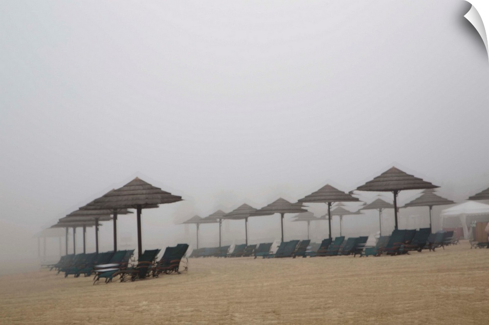 Blurred photograph of a sandy beach lined with beach chairs and umbrellas, created with multiple exposures.