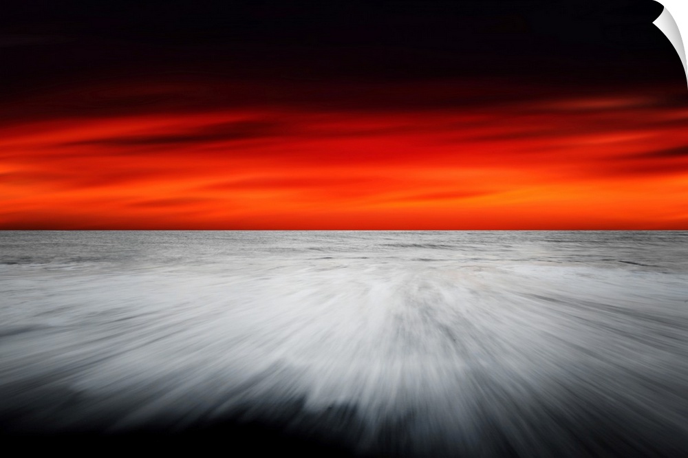 A dramatic photograph of a blazing sky hanging over a white seascape seen from a black sand beach.