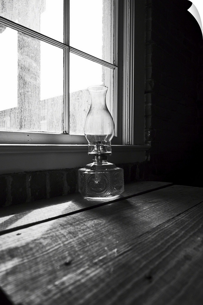 Low angle view of an old glass oil lamp on a wooden desk at a house window.