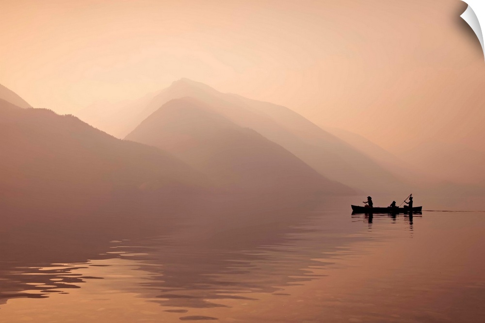 A photograph of people in a rowboat on lake beside mountains in silhouette.