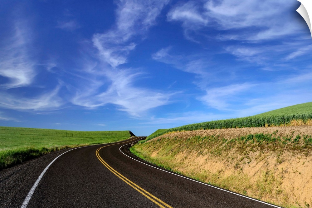 Paved road through the fields of Palouse, Washington, under a blue sky.