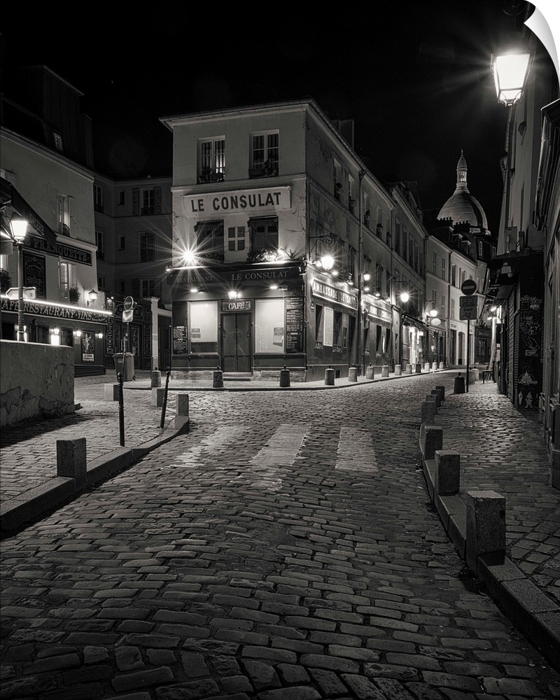 A nightscape in Monmarte, Paris, France showing the famous Le Consulat cafe with wrought iron street lamps and the cobbled...