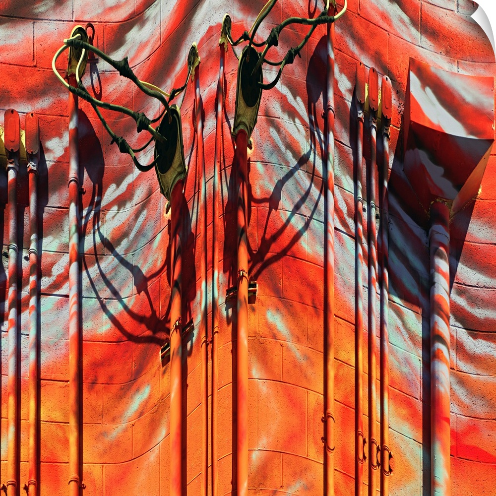 Conceptual photo of red and orange painted pipes and wires on the side of a building, warped to create an abstract image.