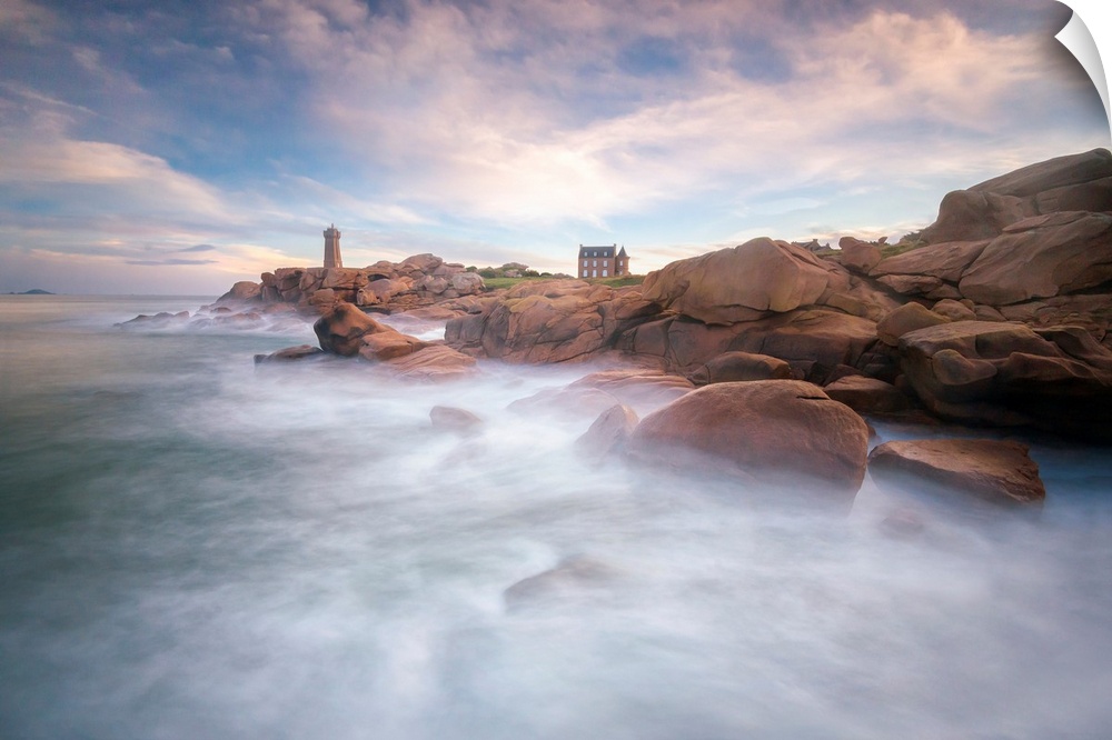 Fine art photo of misty ocean waters at the rocky coast of France with a lighthouse in the distance.