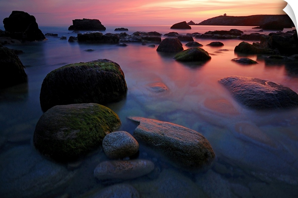 Rocky beach during pink sunset in Brittany, France, big rocks and quite sea at first plan.