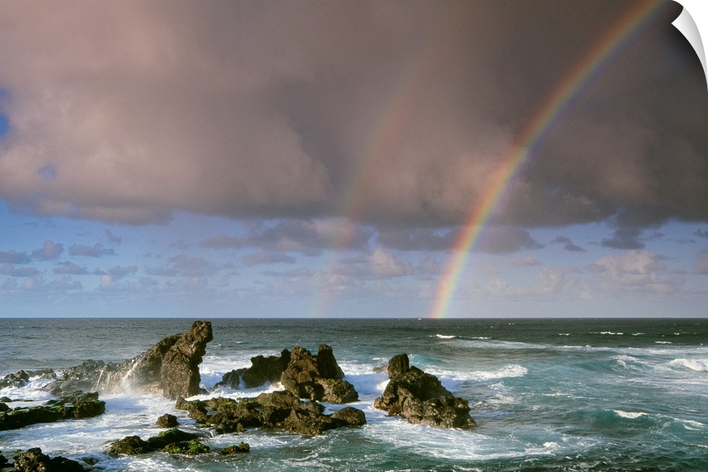 A rare double-rainbow arches across the rocky shore after a storm in a coastal landscape, Maui, Hawaii