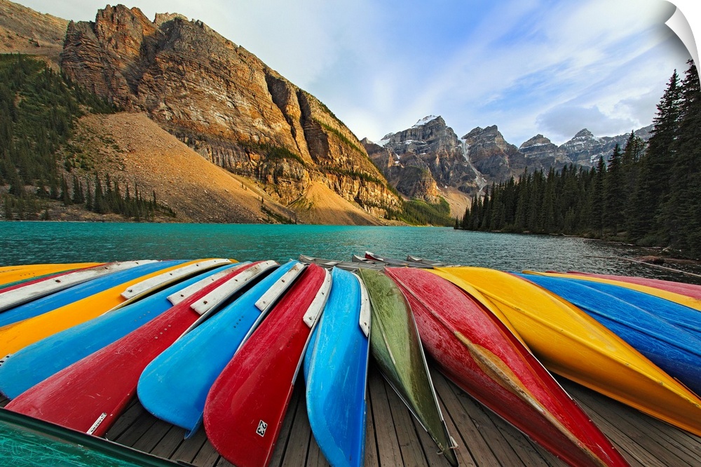 Large, horizontal photograph of colorful boats lined up on a dock at Moraine Lake.  The mountains in Banff National Park, ...